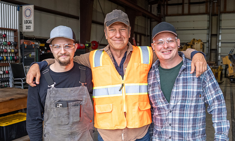 Three smiling men stand together in a workshop