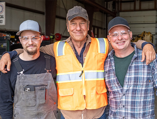 Three men stand smiling with their arms around each other.
