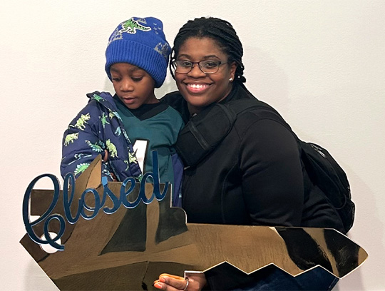 A woman and child stand together holding a large key that says Closed.