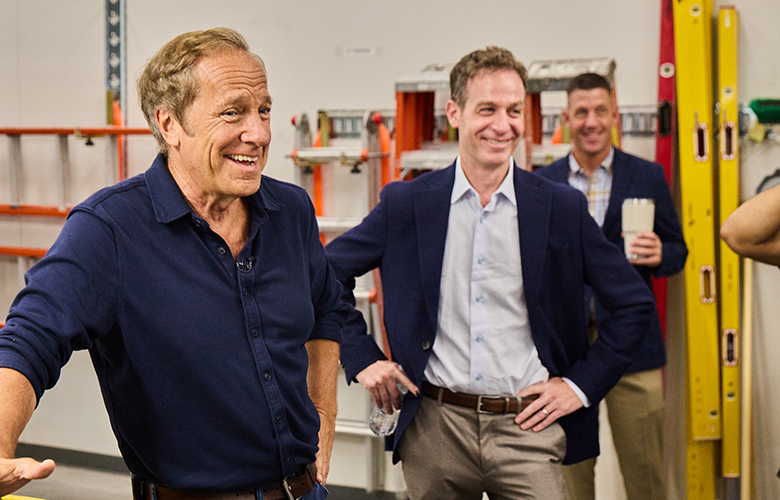 Mike Rowe speaks with attendees inside a construction training facility.