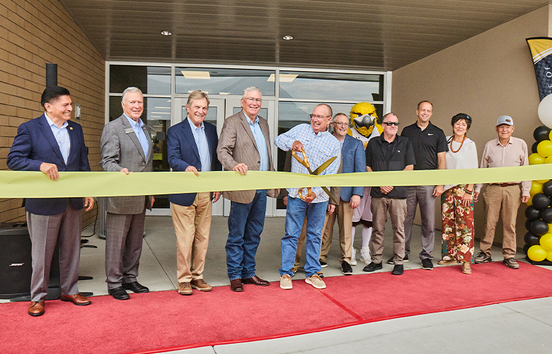 A group gathers outside a building as a ribbon-cutting ceremony takes place.