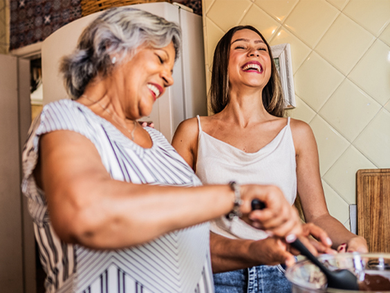 Two women share a laugh while mixing a bowl of batter.