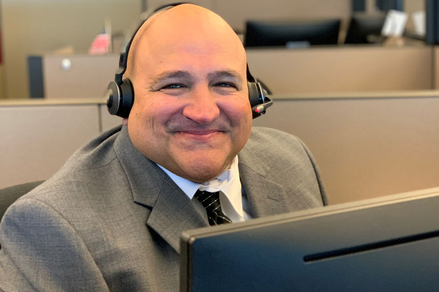 Man wearing a suit sits at computer wearing headphones.