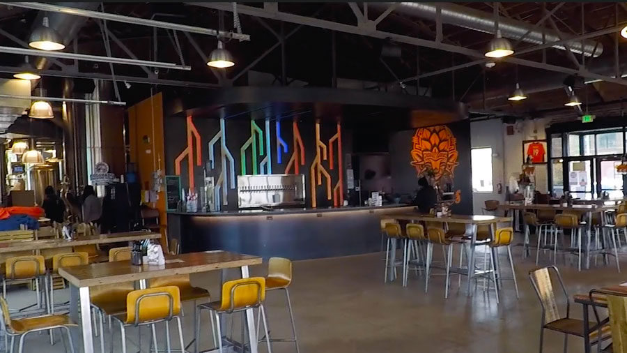 The finished brewery features a bar area with colorful artwork and rows of tables and chairs.