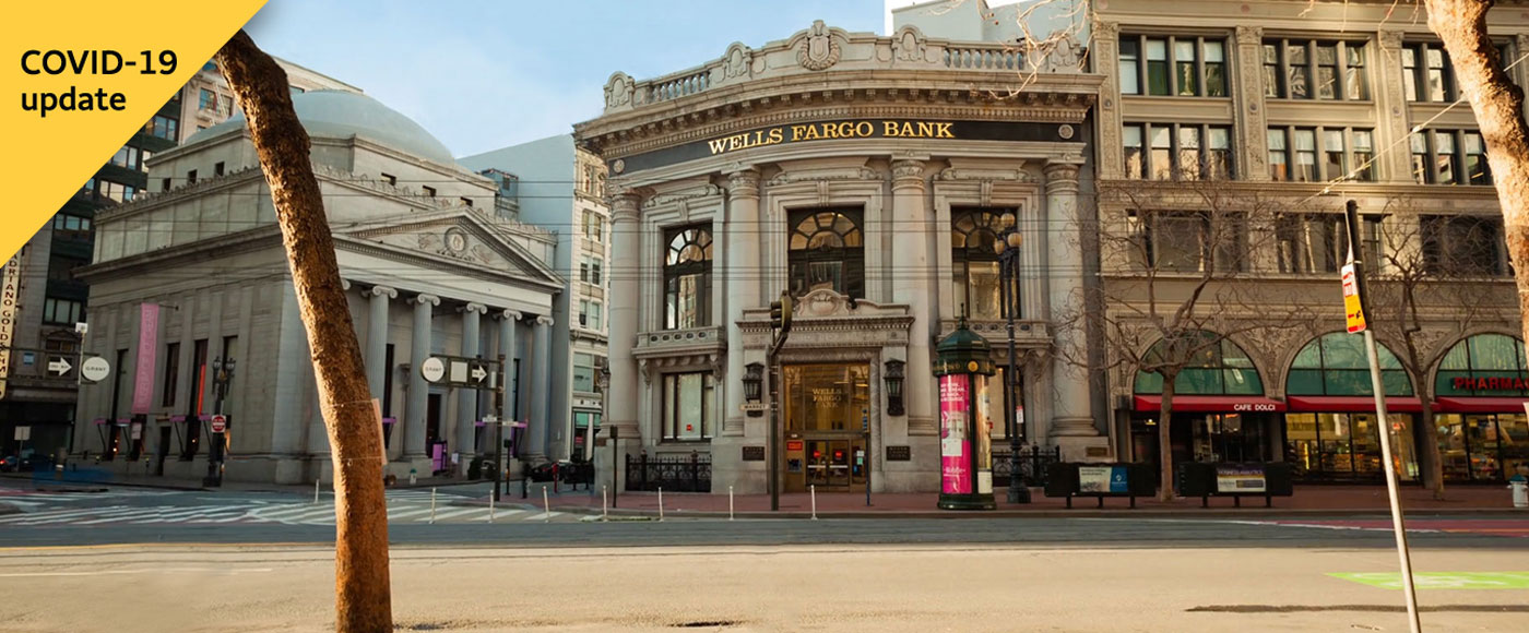 Photo of a Wells Fargo Bank building has a yellow triangle at the top-left corner of the image that says 'COVID-19 update'