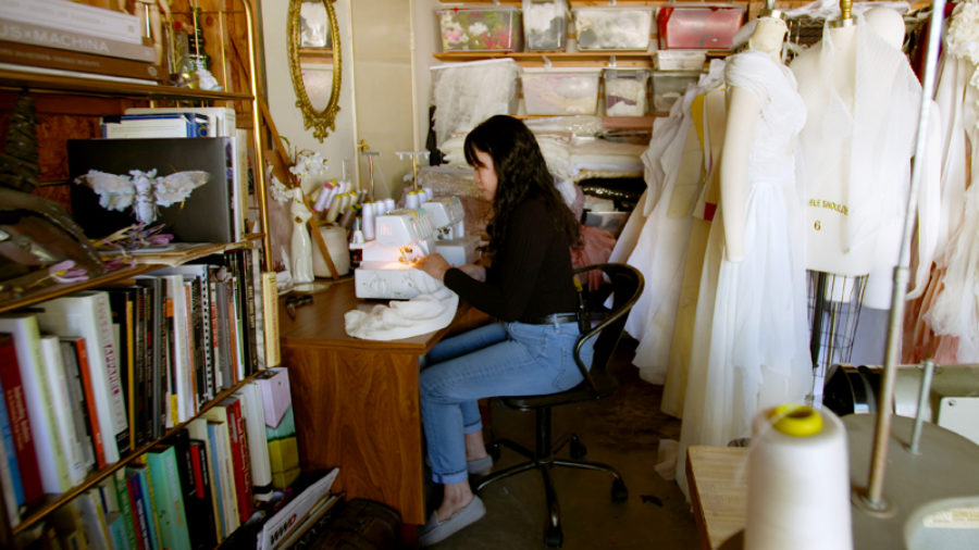 Michelle Hébert sits at serger sewing machine, working on a design.