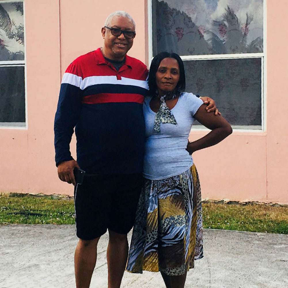 Feliton Gauthier and his wife Mimose stand together in front of their home, smiling with arms around each other.