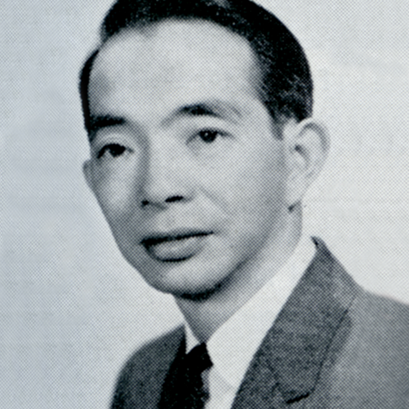 A black and white photo shows the headshot of Lyman Jang wearing a dark suit jacket, a white shirt, and a dark tie. He is looking ahead, slightly off to the right.