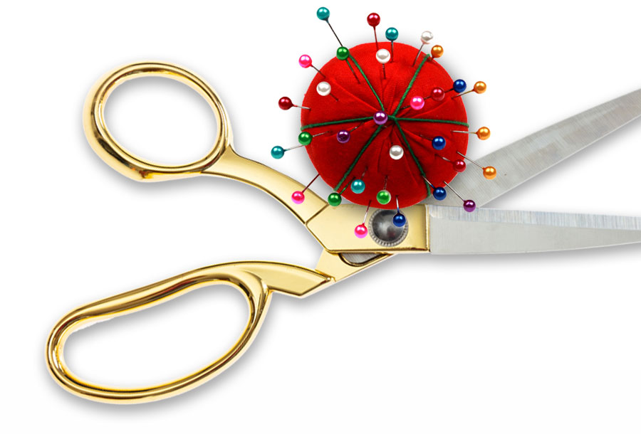 A pair of scissors and a pin cushion with pins in it are in front of a white background.
