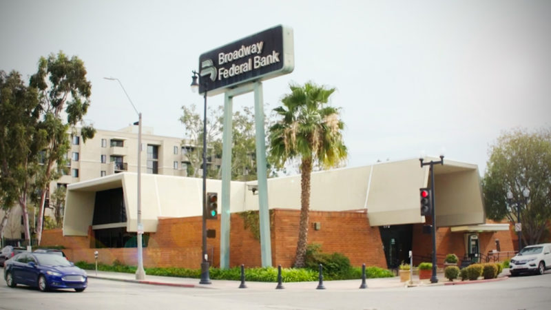 On the corner of the street is a one-story office building with a large sign that reads Broadway Federal Bank.