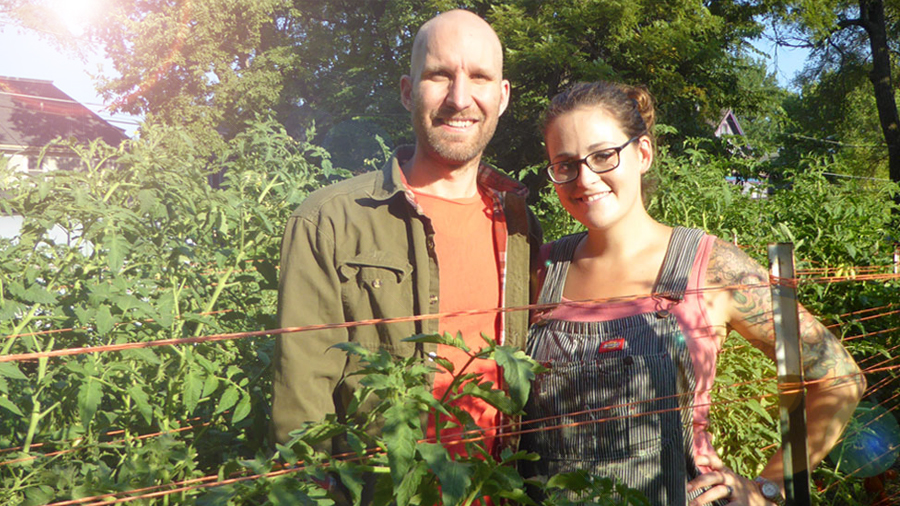 A man and woman stand in a tall garden as they smile at the camera.