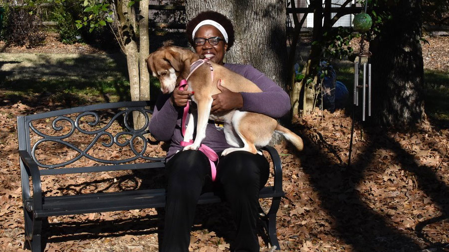 A woman sits on a park bench holding her dog in her lap.