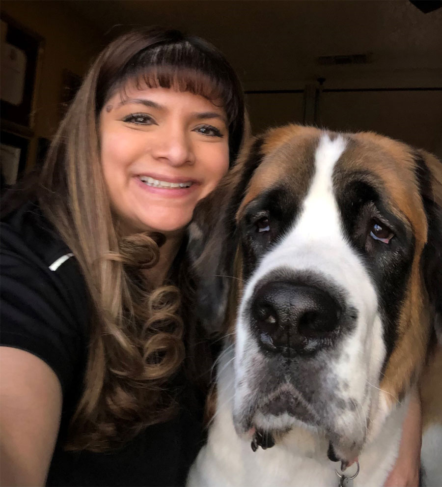 A smiling woman rests her cheek on a large dog’s head.