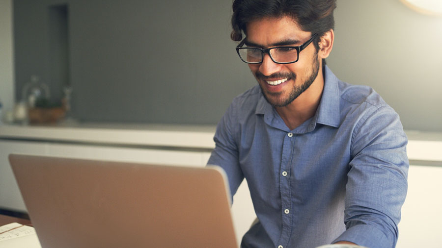 A man smiles as he sits at a laptop.