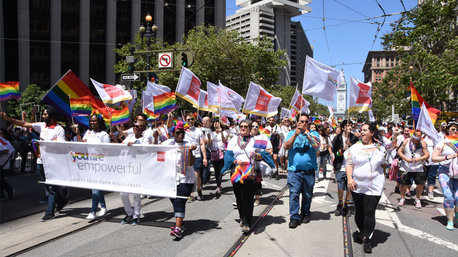 A large group of people march in a Pride parade carrying rainbow flags and a banner that says, 'You're empowerful.'